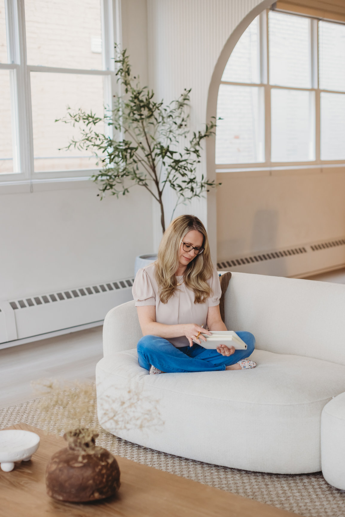 Sarah Hope journaling on a cream bouclé sofa beside large windows in natural light