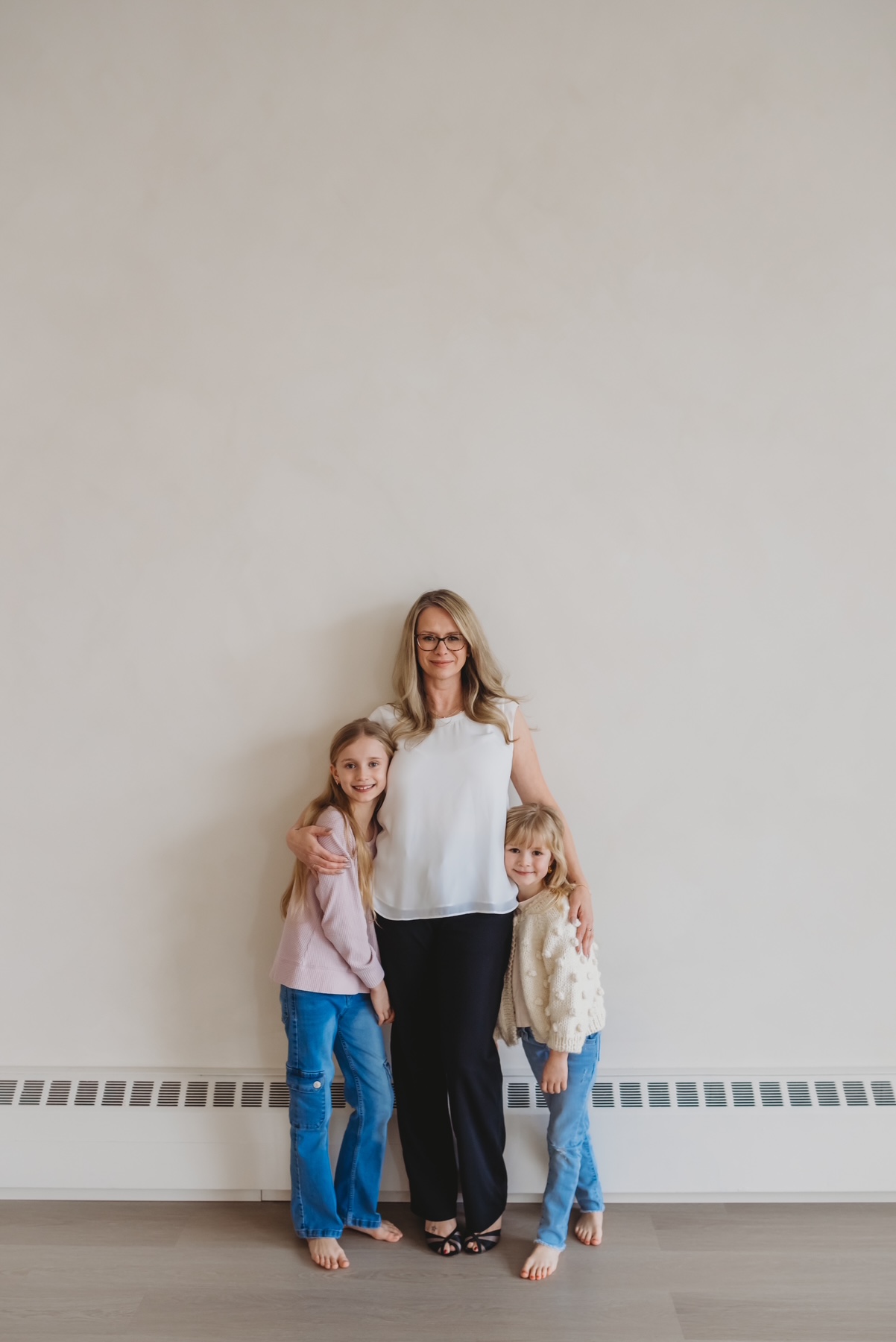 Sarah Hope standing with her two daughters against a warm cream wall, all three smiling